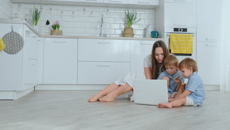 Junge-Schöne-Mutter-Sitzt-Mit-Den-Kindern-Auf-Dem-Boden-Im-Wohnzimmer-Und-Schaut-Auf-Den-Laptop-Bildschirm